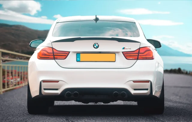Rear view of a white BMW M4 in an edited lakeside setting.